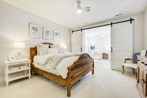 Primary bedroom with upholstered gray bed, vaulted ceiling, and barn doors opening to a stone fireplace sitting room