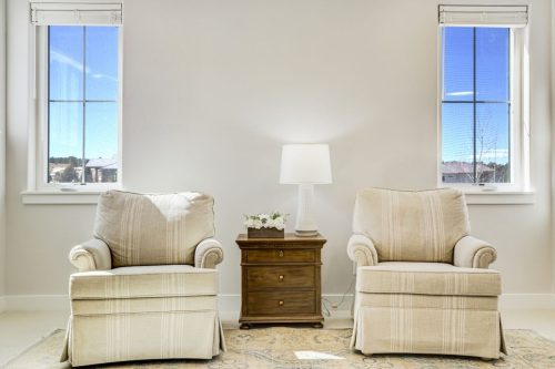 Pair of matching upholstered armchairs flanking a wood nightstand with table lamp and fresh flowers