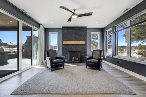 Sunroom with black leather chairs facing a black marble fireplace, surrounded by windows with mountain views