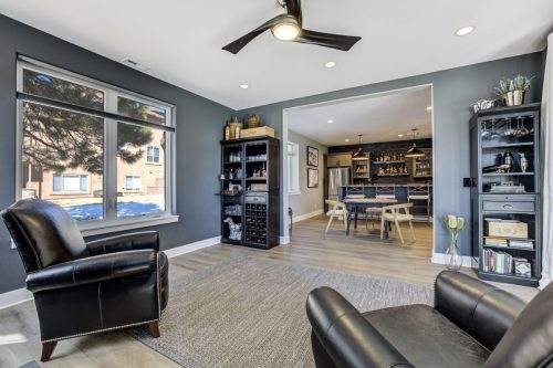 Basement lounge with leather armchairs, black bookshelves, and view into a wet bar and dining area